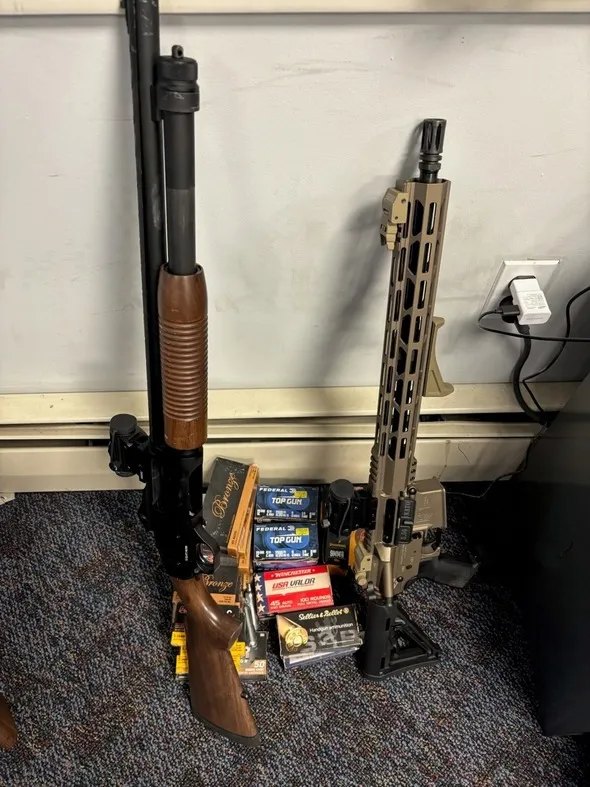 DHS evidence photo: a shotgun, a semi-automatic rifle and boxes of ammunition against a wall